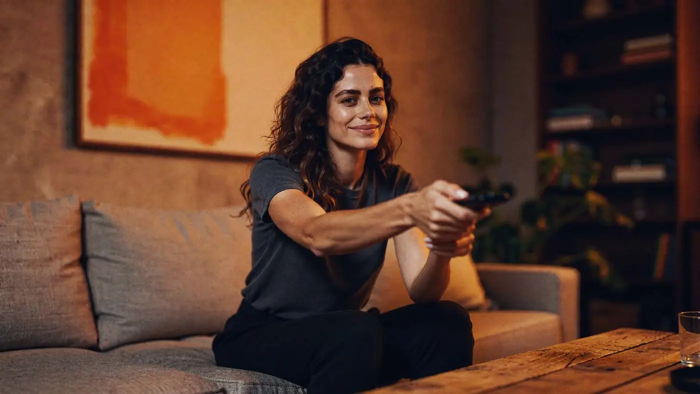 A woman on the sofa, remote in hand, choosing what to watch.